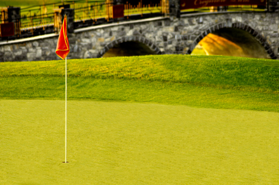 A red flag on a putting green beside a stone bridge at Cregmore Park.