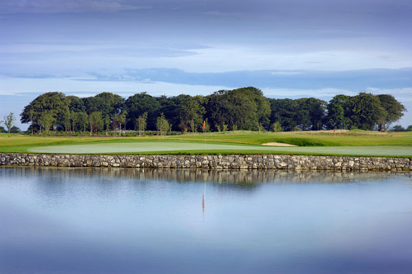 A green and red flag beyond water and a stone retaining wall at Cregmore Park.